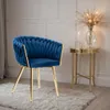 A blue velvet chair with gold legs sits on a fluffy rug next to a small gold side table with a vase of dried flowers and a candle. Náhled obrázku produktu