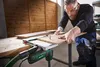 A man is using a jigsaw to cut a piece of wood on a workbench. Produktbild-Vorschau
