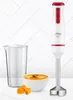 A white and red Ufesa hand blender with a stainless steel base, a clear measuring cup, a bowl of orange soup, and some chopped pumpkin pieces are arranged on a white surface with a white tiled background. Voir les images du produit