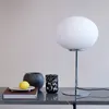 A table lamp with a white globe shade and chrome base is displayed on a dark marble countertop, alongside decorative objects. Produktbild-Vorschau