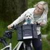 A woman is riding a bicycle with a dog in the front basket. Produktbild-Vorschau