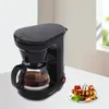 A black coffee maker sits on a white table next to a plate of waffles. Produktbild-Vorschau