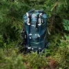 A green backpack with hiking poles attached, set in a forest. Anteprima dell’immagine prodotto