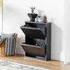A dark gray shoe cabinet with two flip-down drawers is shown in a room with a basket of blankets to the left and a wall to the right.