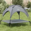 A gray dog bed with a canopy is set up on a grassy lawn in front of a wooden fence and some bushes. Anteprima dell’immagine prodotto