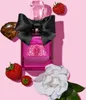A Juicy Couture Viva La Juicy Noir eau de Parfum bottle is surrounded by strawberries and a white flower on a pink background. Podgląd zdjęcia produktu