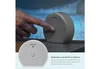 A hand is shown pressing a button on a small, round, gray device, with another similar device in the foreground. Text is present on the right side. Voir les images du produit