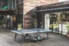 An outdoor ping pong table is set up on a wooden deck next to a modern wooden house. Produktbild-Vorschau