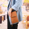 A person wearing a blue jacket is holding a brown crossbody bag. Produktbild-Vorschau
