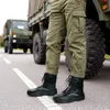 A person wearing work boots and cargo pants stands on a road next to a large military truck. Náhled obrázku produktu