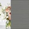A bouquet of flowers in a vase is partially obscured by a gray pleated blind. Produktbild-Vorschau