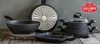 A collection of Ballarini cookware, including pots and pans, arranged on a wooden surface against a textured gray background. Náhľad obrázku produktu