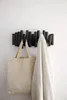 A black coat rack with multiple pegs is mounted on a white wall. A beige tote bag and a cream-colored blanket are hanging from the pegs. Anteprima dell’immagine prodotto