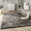 A living room scene with a large gray rug in the foreground, a sofa with a blanket and pillow, a white cabinet, and a shelving unit. Anteprima dell’immagine prodotto