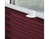 A close-up view of a burgundy pleated blind attached to a white window frame with a clamp mechanism. Produktbild-Vorschau