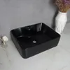 A black washbasin is placed on a marble countertop, with a vase of dried flowers in the background. Podgląd zdjęcia produktu