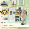 A child is playing with a toy kitchen set, which includes a refrigerator, oven, stovetop, and sink. The kitchen set is decorated with colorful accents and has various accessories. The background shows a room with artwork on the wall. Produktbild-Vorschau