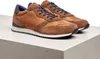 A pair of brown leather and suede sneakers with blue laces and accents, placed on a concrete surface. Produktbild-Vorschau