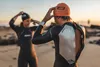 Two people in wetsuits on a beach at sunset, preparing for a swim. Produktbild-Vorschau