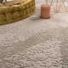 A close-up view of a shaggy rug with a textured surface, a yellow pouf, and a candle in the foreground. Voir les images du produit
