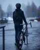 A person in a helmet and jacket stands with a bicycle on a wet road. Produktbild-Vorschau