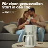 A couple is sitting on a couch, holding coffee cups, with a coffee maker in the foreground. Anteprima dell’immagine prodotto