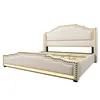 A beige upholstered bed frame with gold stud accents, presented on a white background. Náhled obrázku produktu