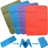 Four folded foam seat cushions in different colors are fanned out, with a diagram below showing how a blue cushion folds. Produktbild-Vorschau