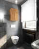 A modern bathroom with concrete walls, a wall-mounted toilet, a wooden cabinet, and a radiator under a window with blinds. Voir les images du produit