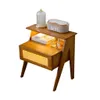 A wooden bedside table with a drawer and shelf, decorated with items like a lamp, clock, and perfume bottles. Náhled obrázku produktu