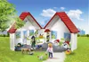 A Playmobil veterinary clinic playset set in a grassy outdoor environment with trees and buildings in the background. Produktbild-Vorschau