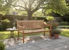 A wooden garden bench sits on a stone patio in a sunny garden, with potted plants and a tree in the background. Produktbild-Vorschau