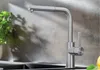 A modern kitchen faucet with a pull-out spout is shown in a close-up shot, with a plant and a sink visible in the background. Produktbild-Vorschau