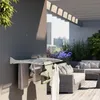 A wall-mounted drying rack with towels and clothes hanging on it, on a balcony with outdoor furniture and city buildings in the background. Produktbild-Vorschau