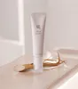 A tube of eye serum is placed on a light-colored surface, with a piece of ginseng root beside it. Voir les images du produit