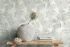 A vase with a dried flower and a stack of books on a wooden shelf against a tropical leaf patterned wallpaper. Produktbild-Vorschau