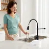 A woman is using a kitchen faucet to rinse a small rectangular object under running water in a kitchen sink. Podgląd zdjęcia produktu