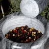 A close-up of a granite mortar and pestle filled with peppercorns. Voir les images du produit