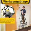 A man is painting a wall while standing on a step ladder with a tool tray. Anteprima dell’immagine prodotto