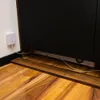 A white smart sensor is plugged into a wall outlet next to a large black appliance, with a wooden plank on the floor in front of the appliance. Podgląd zdjęcia produktu