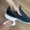A hand is cleaning the sole of a blue sneaker with a white wipe. Produktbild-Vorschau