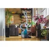 A teal and black vacuum cleaner is positioned on a wooden floor in a living room setting. Produktbild-Vorschau
