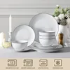 A set of white porcelain dishes with a black rim is arranged on a table, with decorative elements like candles and flowers in the background. Below the dishes, there are icons indicating product features. Produktbild-Vorschau