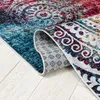 A close-up view of a rug, showing the texture and pattern. The rug is partially rolled up, revealing its underside and a patterned backing. The rug is placed on a light-colored wooden floor. Podgląd zdjęcia produktu