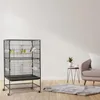A bird cage with birds inside, placed in a living room setting next to a sofa and a small table with a plant. Produktbild-Vorschau