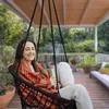 A woman is relaxing in a hanging chair on a wooden deck, holding a mug. Voir les images du produit