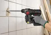 A person wearing gloves is using a cordless hammer drill to break through a tiled wall. Produktbild-Vorschau