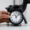 A hand is adjusting a retro analog alarm clock with double bells. Voir les images du produit
