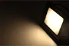 A square LED floodlight is angled towards the viewer, casting a bright warm white light onto a dark surface. Náhled obrázku produktu