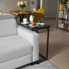 A modern living room scene with a sofa, a C-shaped side table, and a dining area in the background. Produktbild-Vorschau